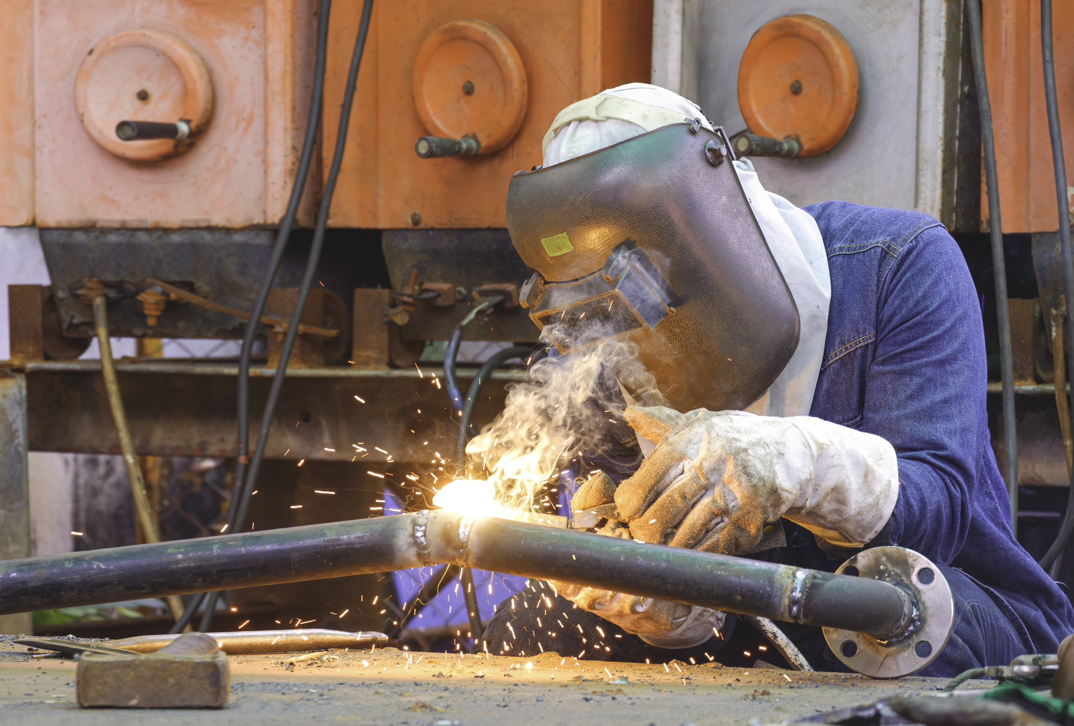 Welder with safety equipment is welding steel pipe at workshop for use in oil pipeline system renovate work in tanker ship